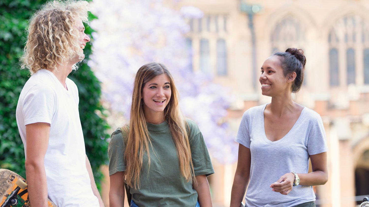 Two women and a man with curly hair talking and smiling in a university setting.