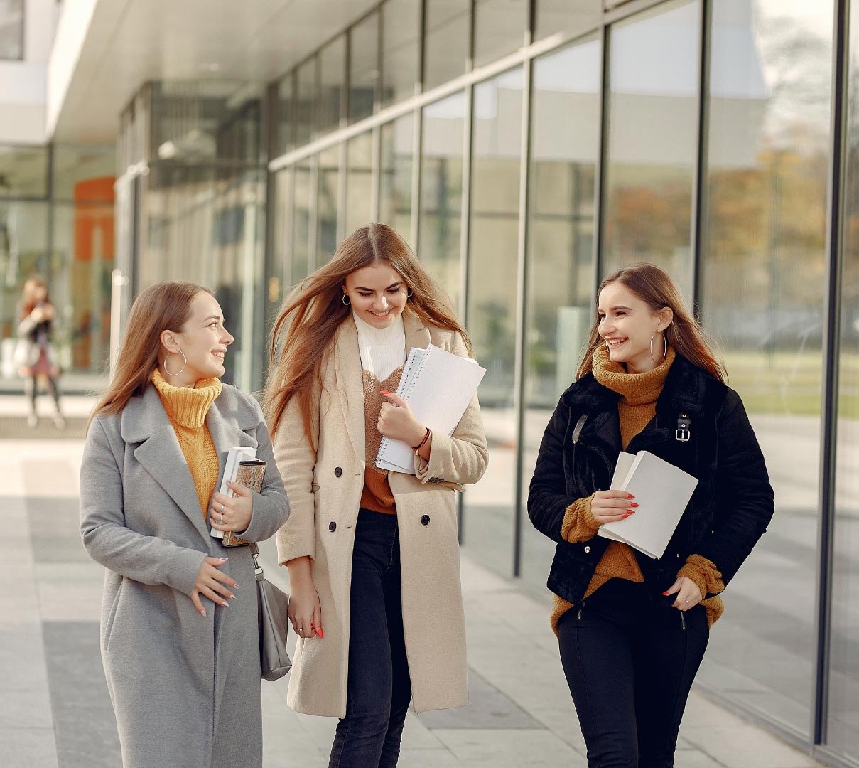 Three female students walking and talking outside a modern university campus.