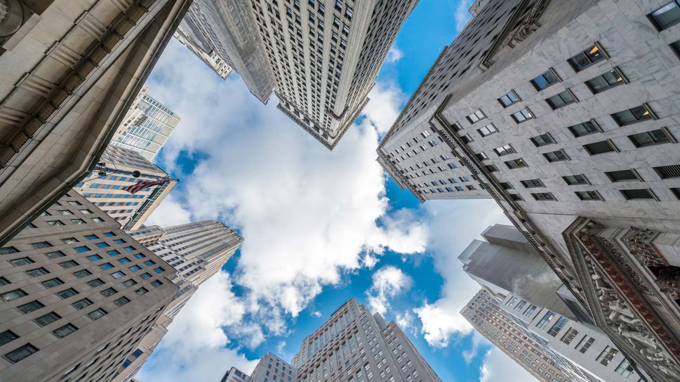 Looking up at towering skyscrapers under a blue sky with clouds in New York City.