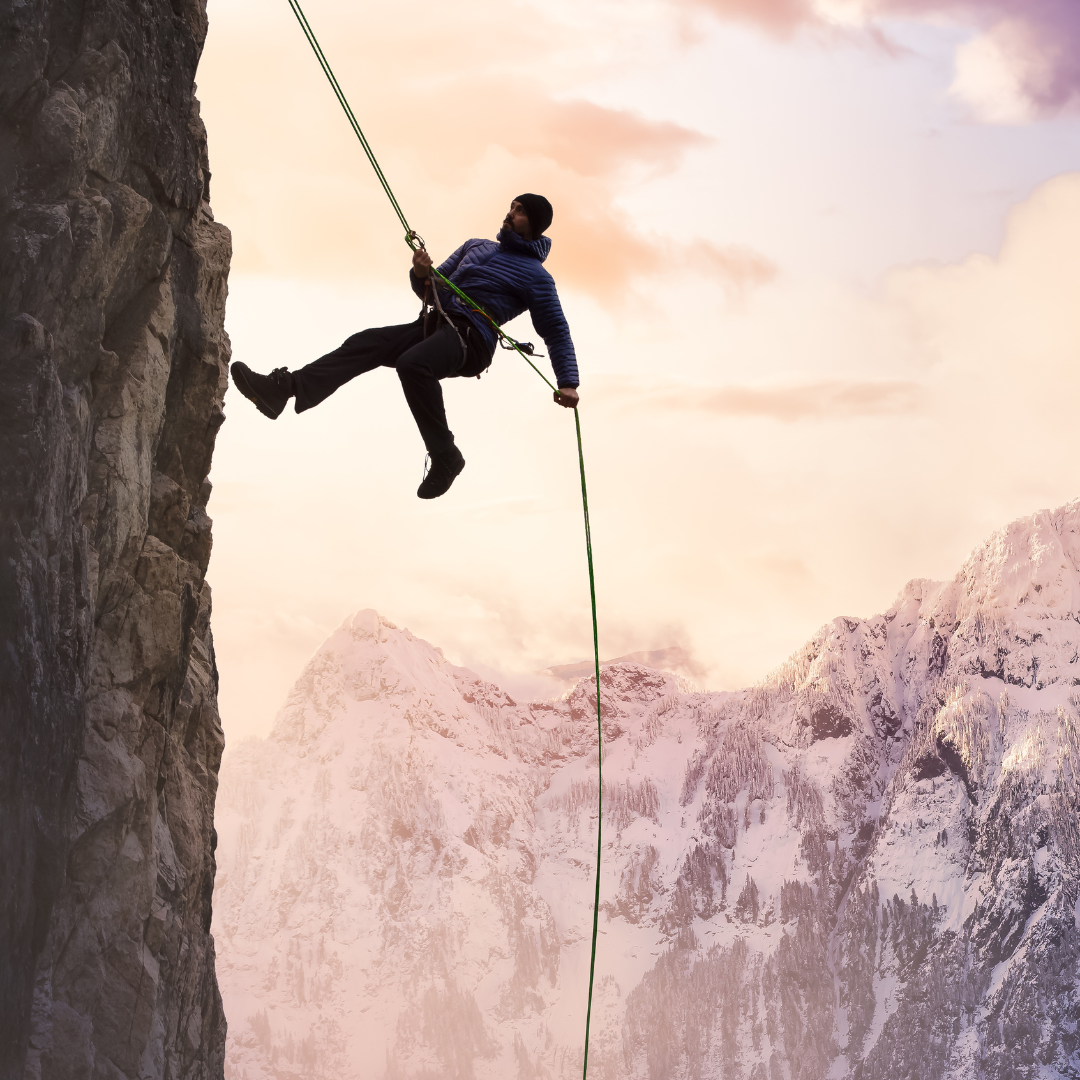 Mountain Climber going up sheer rock face with rope. Mountain in the background