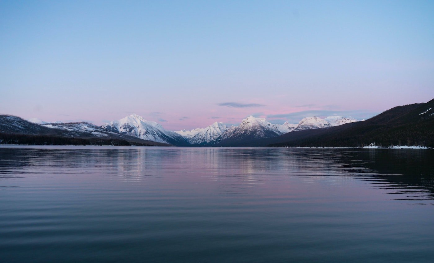 A lake reflecting a cotton candy sunset behind mountains
