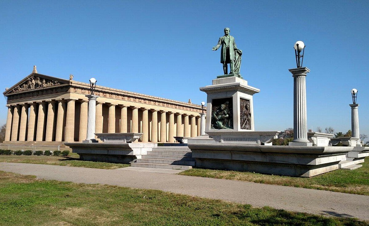 A full-scale replica of the Parthenon with a statue in front, under a clear blue sky.