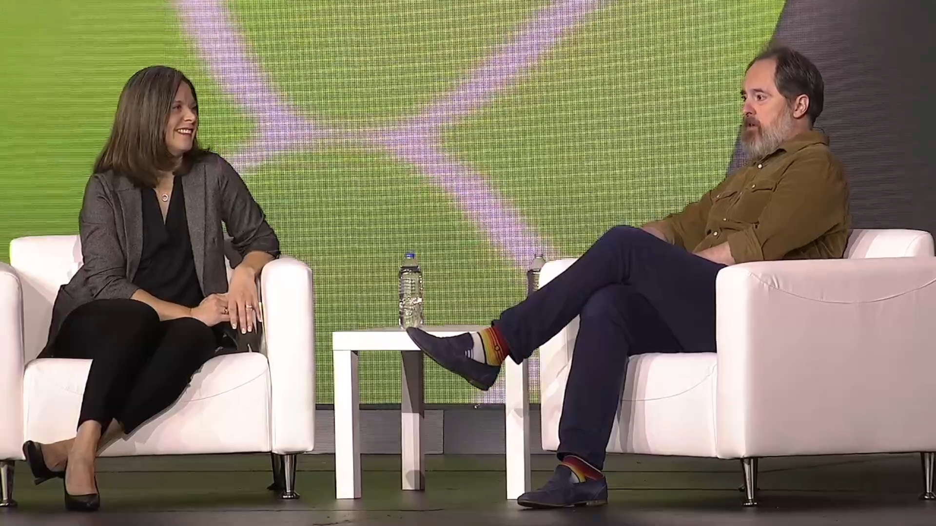 Two people sitting on white chairs on a stage (Hannah Grap, Sitecore and Brendan Hunt, actor) at Sitecore Symposium 2024 in Nashville