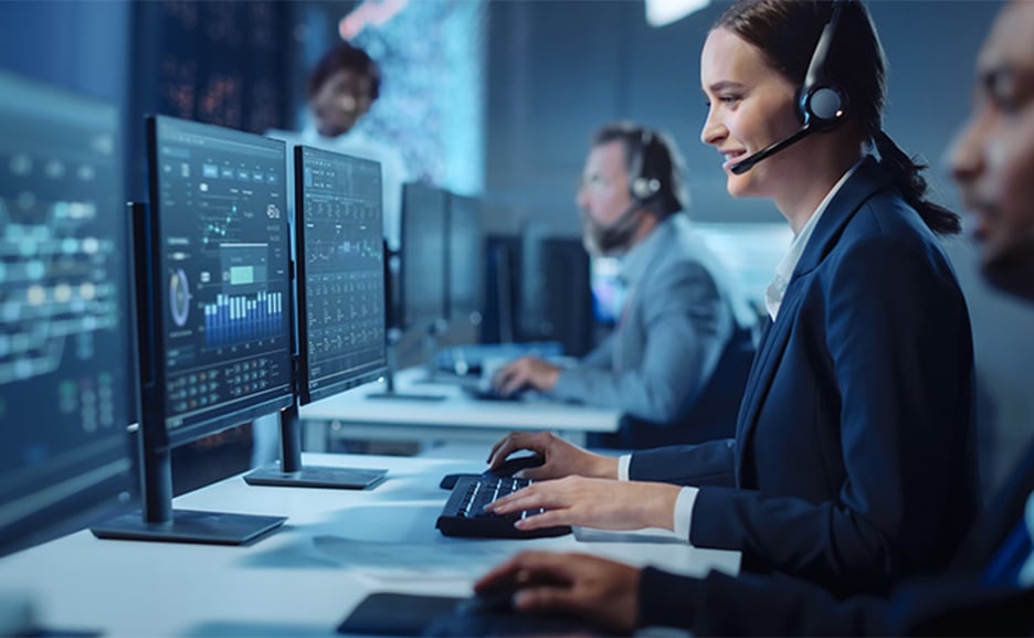 ヘッドセットをつけた女性が、複数のモニターにデータが表示されたコンピューターを操作している様子