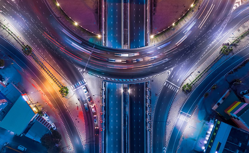 Aerial view of a highway junction at night with light trails from cars.