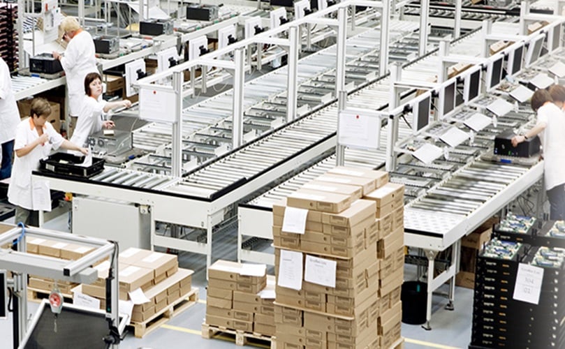 Inside a factory, multiple employees are actively working on the production floor, surrounded by machinery.