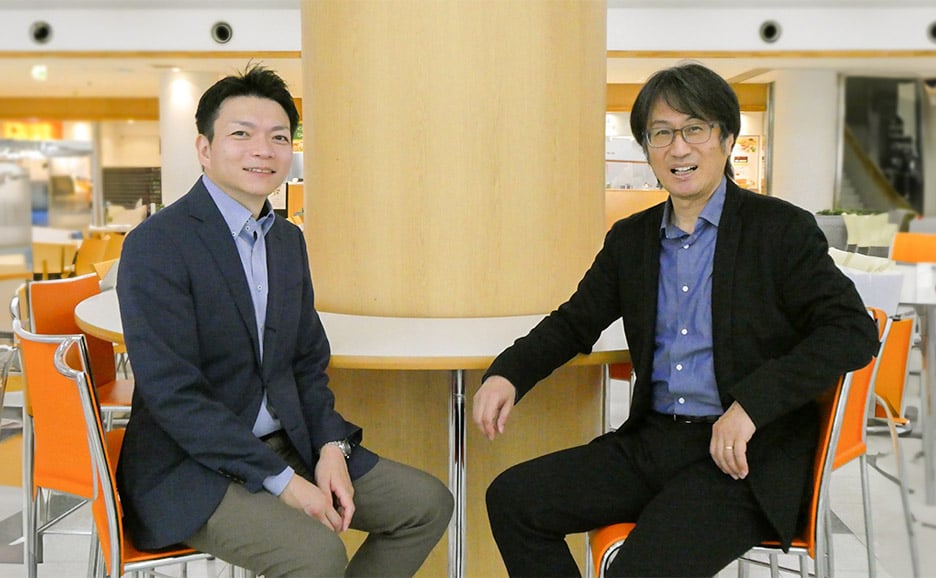 東洋大学社会学部長の桐生教授と、富士通の紺野が、大学の食堂で二人並んで座っている写真