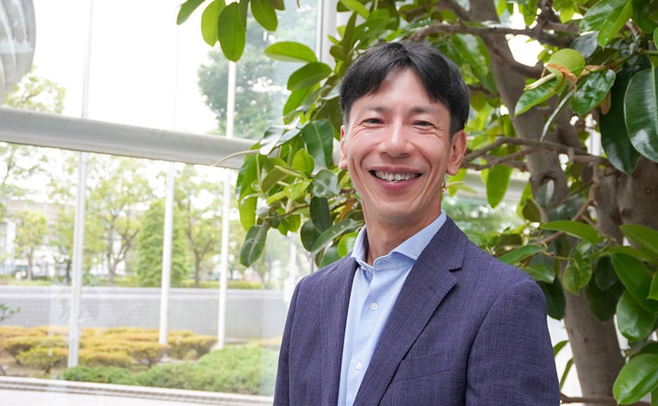 富士通株式会社 技術戦略本部 コミュニケーション戦略統括部 シニアディレクター 西川 博が緑の多いオフィスの前にて、笑顔で写る写真