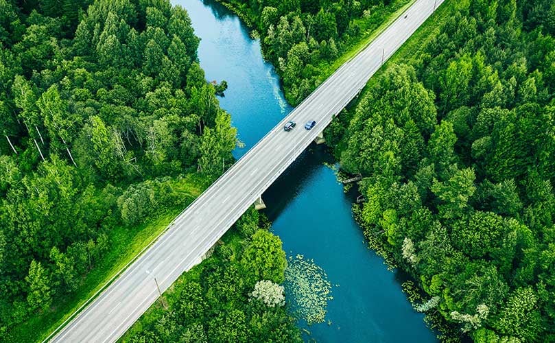 An aerial view of cars crossing a bridge over a river flowing through a forest.