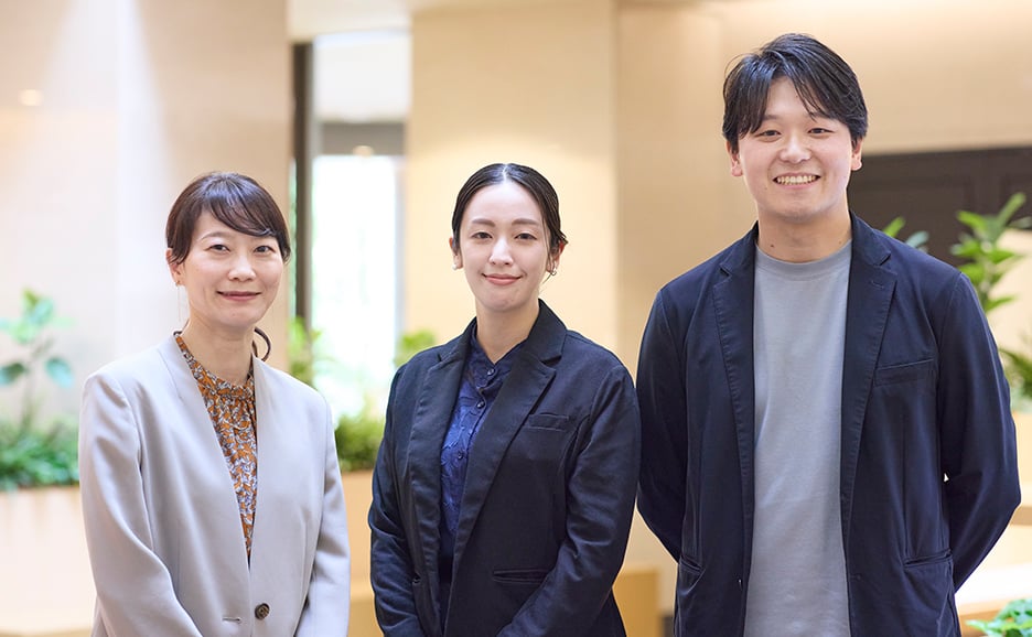 明るい室内で、笑顔で並んで立つスーツ姿のビジネスパーソンたち