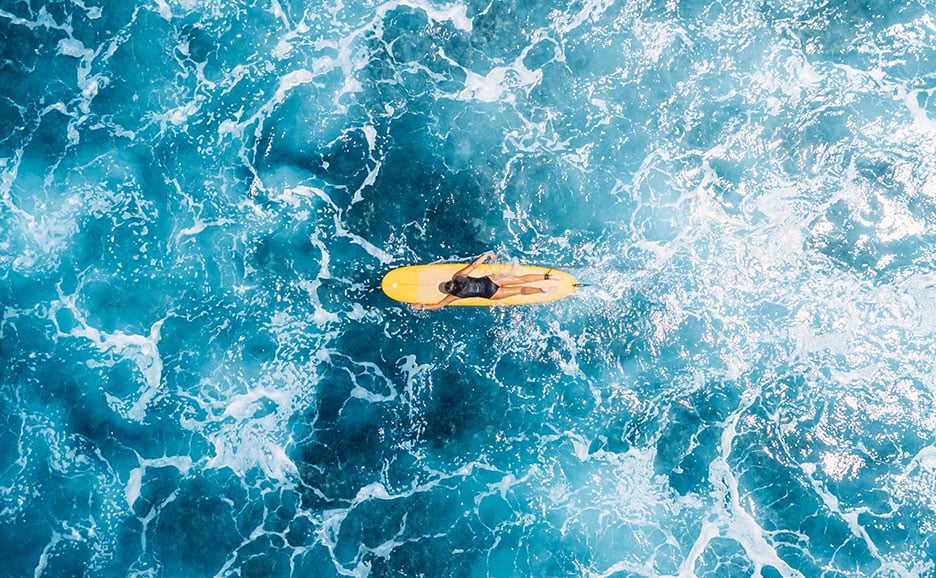 A person lies on a yellow surfboard above blue ocean waves.