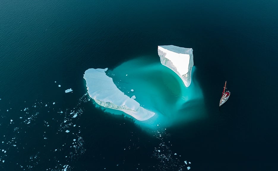 暗い海に浮かぶ二つの氷塊のそばを帆船が進む。