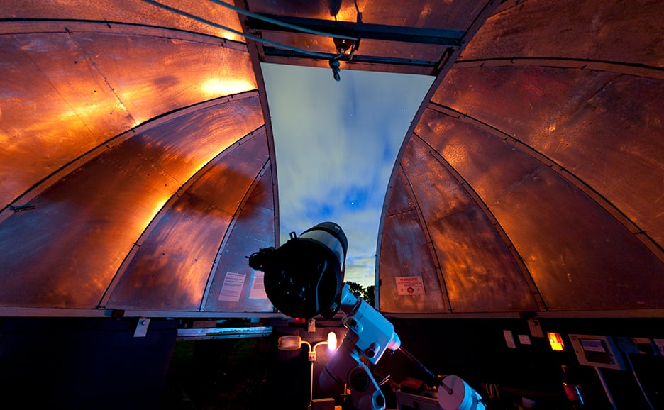 Inside an observatory dome with a telescope pointed at the night sky.