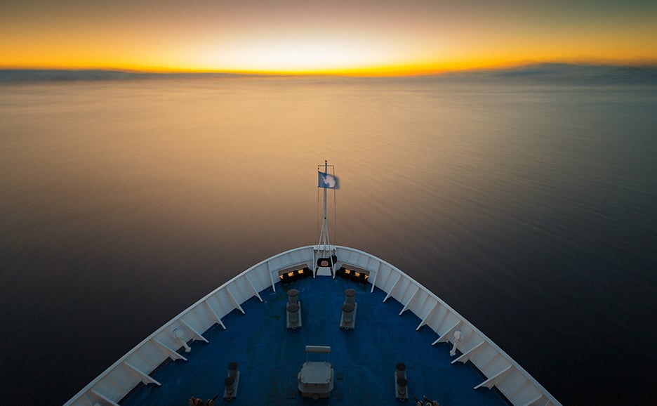 View from a ship's bow of the open sea and sunset on the horizon.