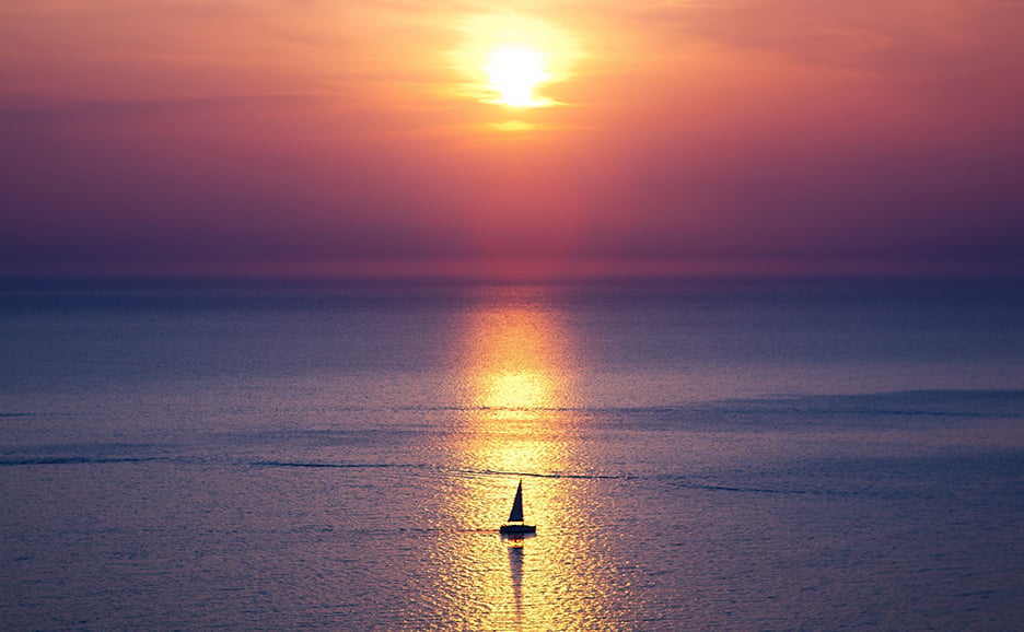 Silhouette of a sailboat on the water reflecting the sunset, against a sunset sky and sea.