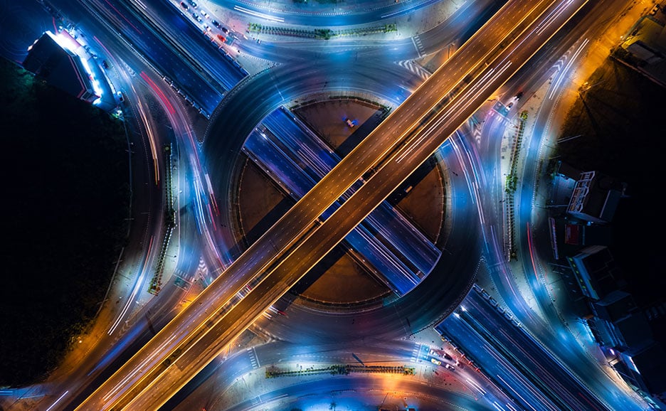 夜景のインターチェンジで、オレンジの高速道路と青い一般道が交差している。