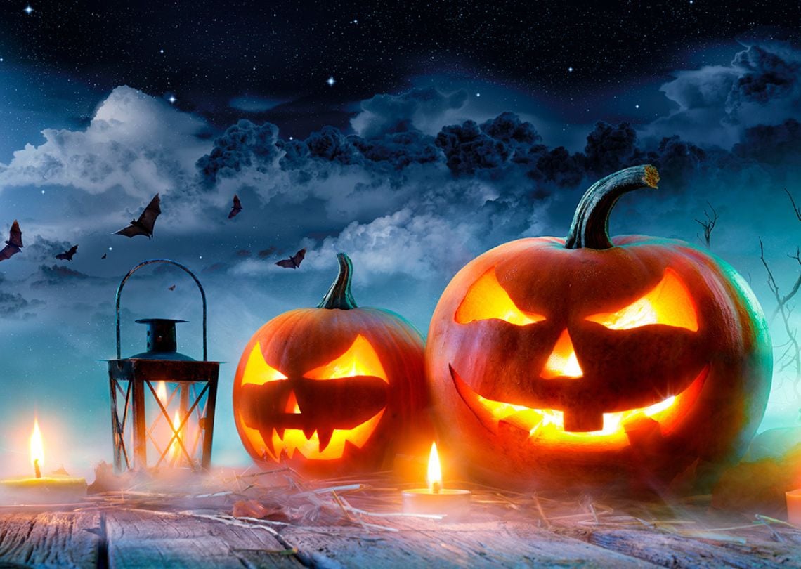 Fantástica cena de Halloween com abóboras iluminadas, lanternas e um céu noturno repleto de nuvens e morcegos, criando um ambiente assustador.