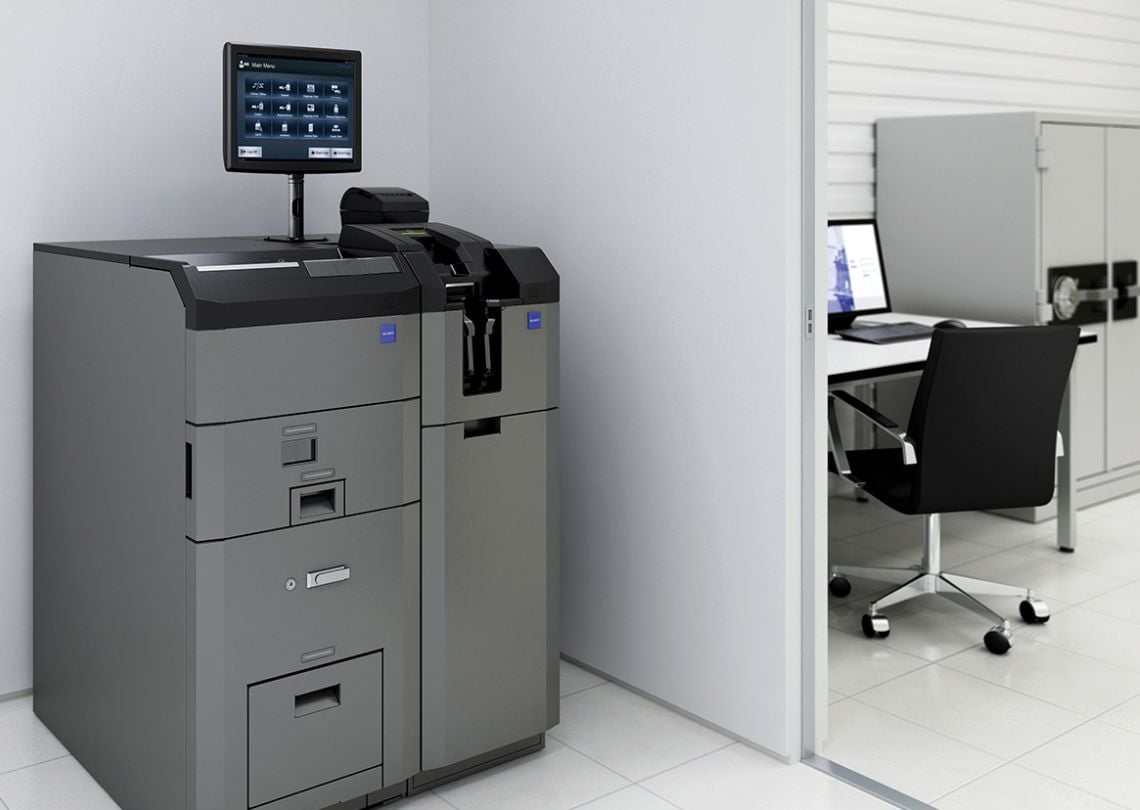 Autoatendimento em ambiente corporativo, com monitor digital e mesa de trabalho ao fundo.