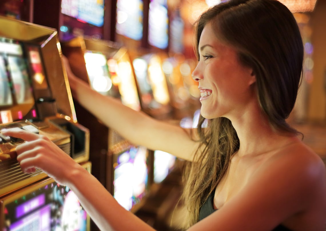 Mulher sorridente jogando em uma máquina caça-níqueis em um cassino, com iluminação brilhante ao fundo, simbolizando diversão e entretenimento.