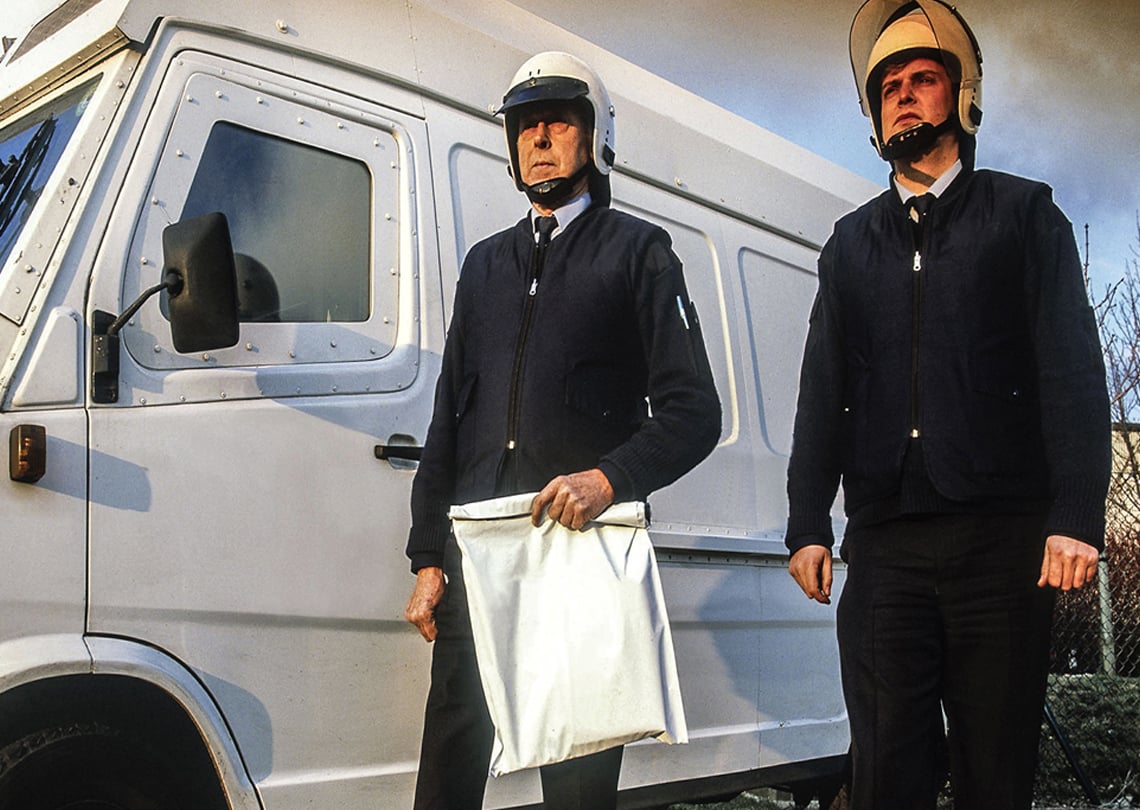 Homens em uniforme ao lado de uma van branca, simbolizando serviços de segurança ou transporte de valores.