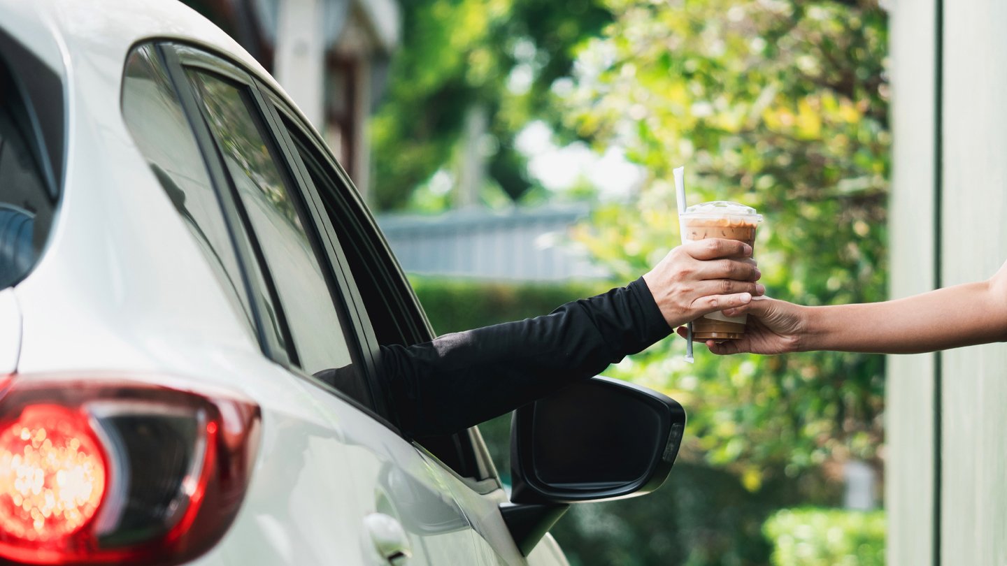 Pessoa recebendo um copo de bebida gelada em um drive-thru, mostrando o serviço rápido e prático dessa experiência.