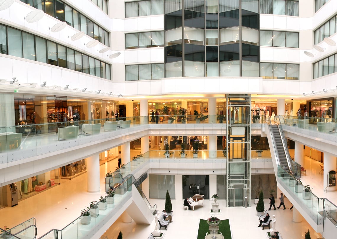 Vista interna de um shopping moderno com várias lojas, escadas e área de descanso, oferecendo uma atmosfera luxuosa e convidativa. Ideal para compras e passeios.