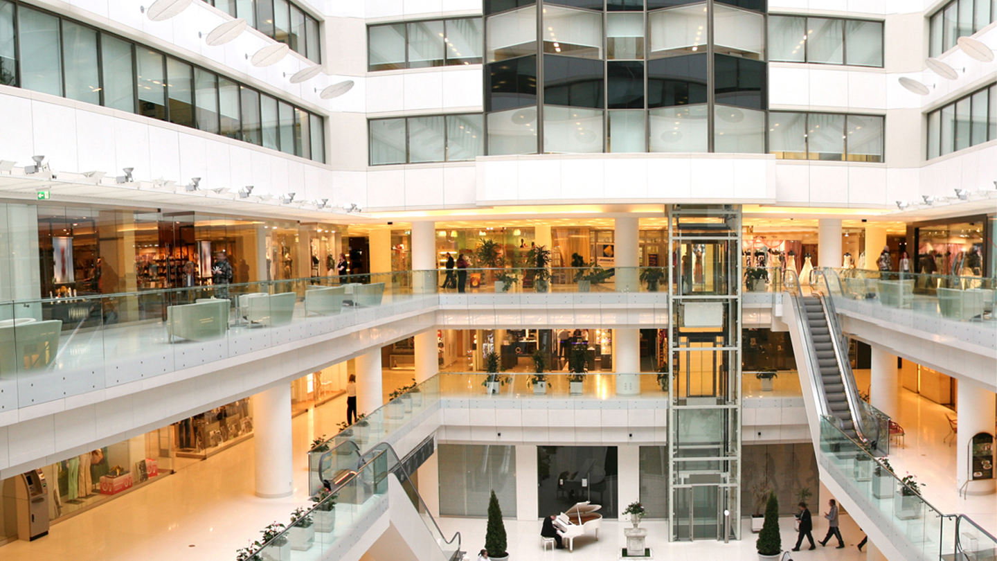 Vista interna de um shopping moderno, com várias lojas, escadas rolantes e um design contemporâneo. Um ótimo exemplo de arquitetura comercial.