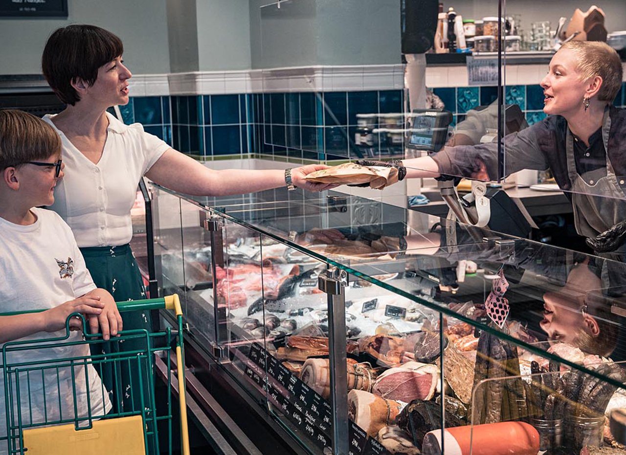 Kassiererin übergibt Produkt an der Fleischtheke