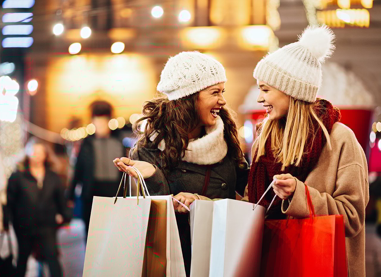 Zwei glückliche Freund:innen kaufen Weihnachtsgeschenke ein