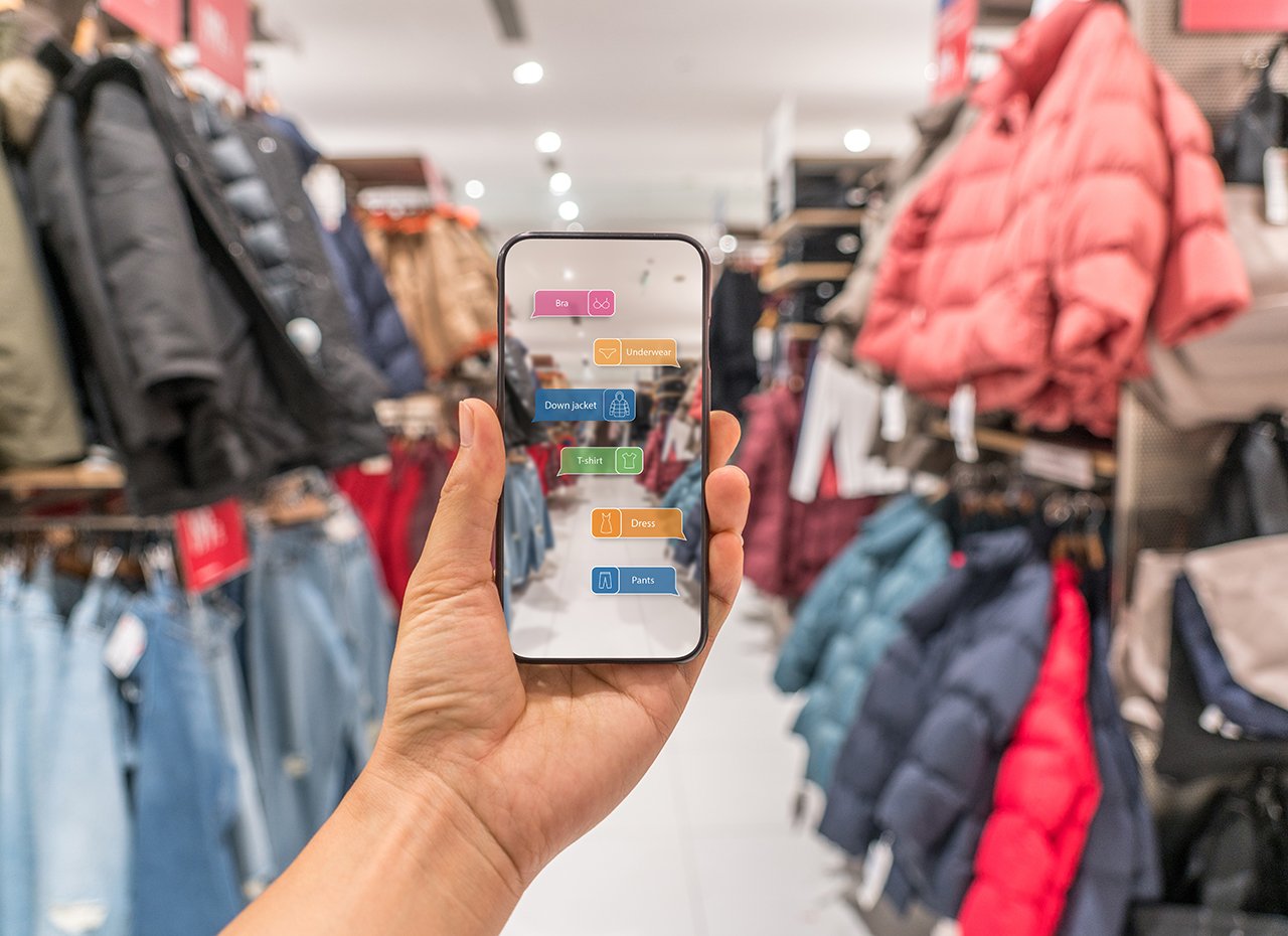 Eine Hand hält ein Handy vor einem Bekleidungsgeschäft