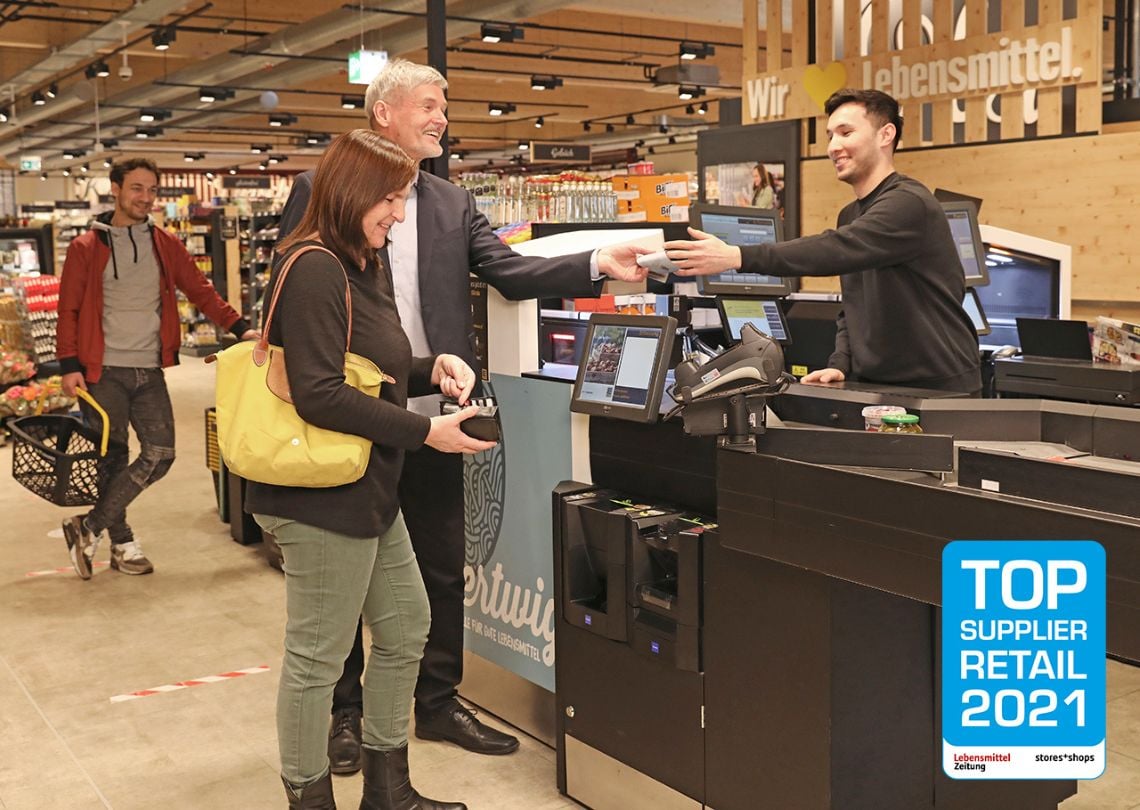 Imagem de um cliente satisfeita recebendo atendimento no caixa de um supermercado moderno, destacando a interação entre funcionários e consumidores.