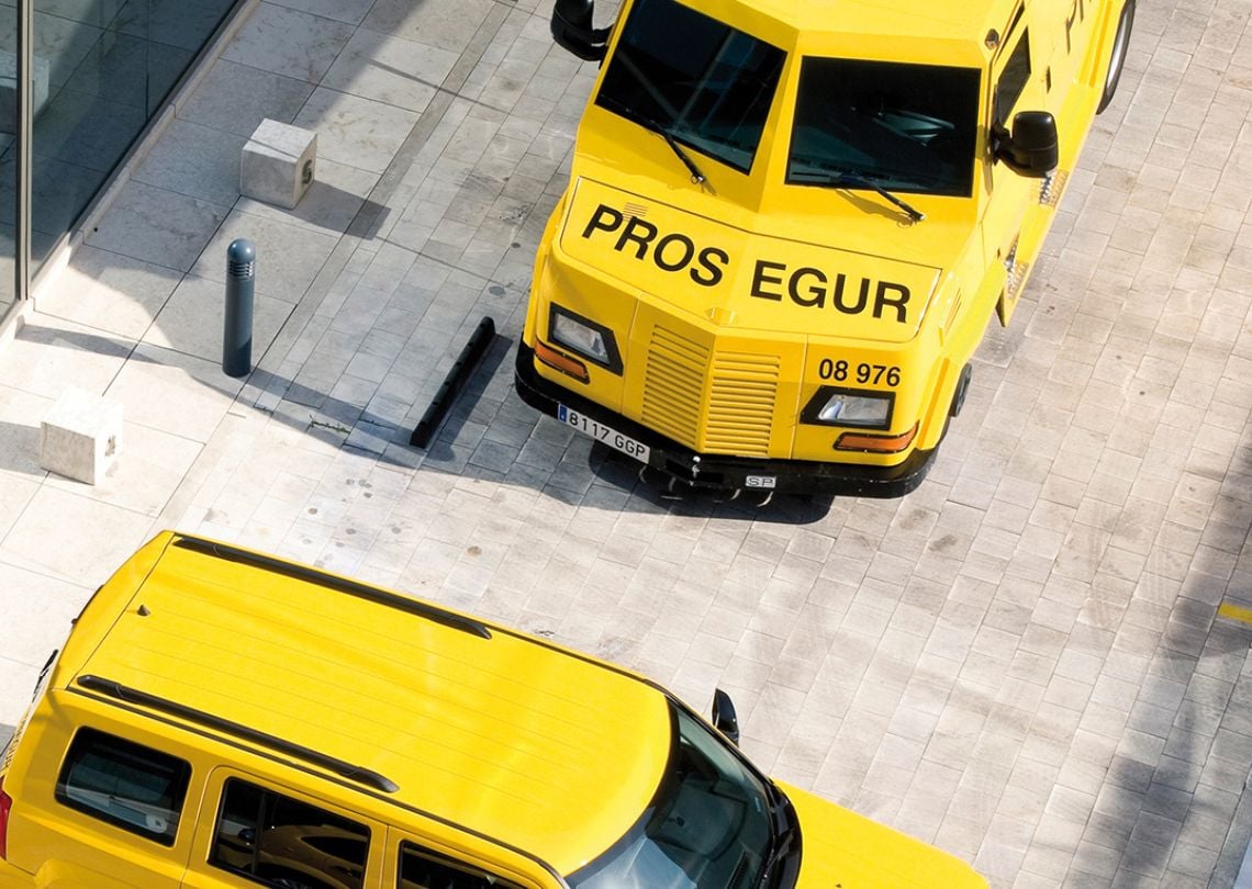 Imagem de veículos de segurança amarelos estacionados, destacando um caminhão com a inscrição 'PROS EGUR'. Perfeito para identificar transporte de segurança.