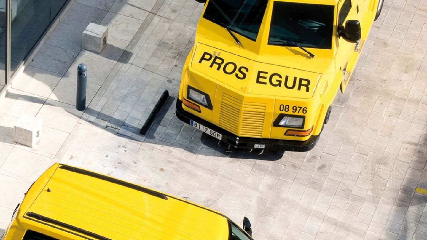 Imagem de veículos de transportadoras de valores amarelos estacionados em uma área urbana, mostrando detalhes distintos de design e cores.