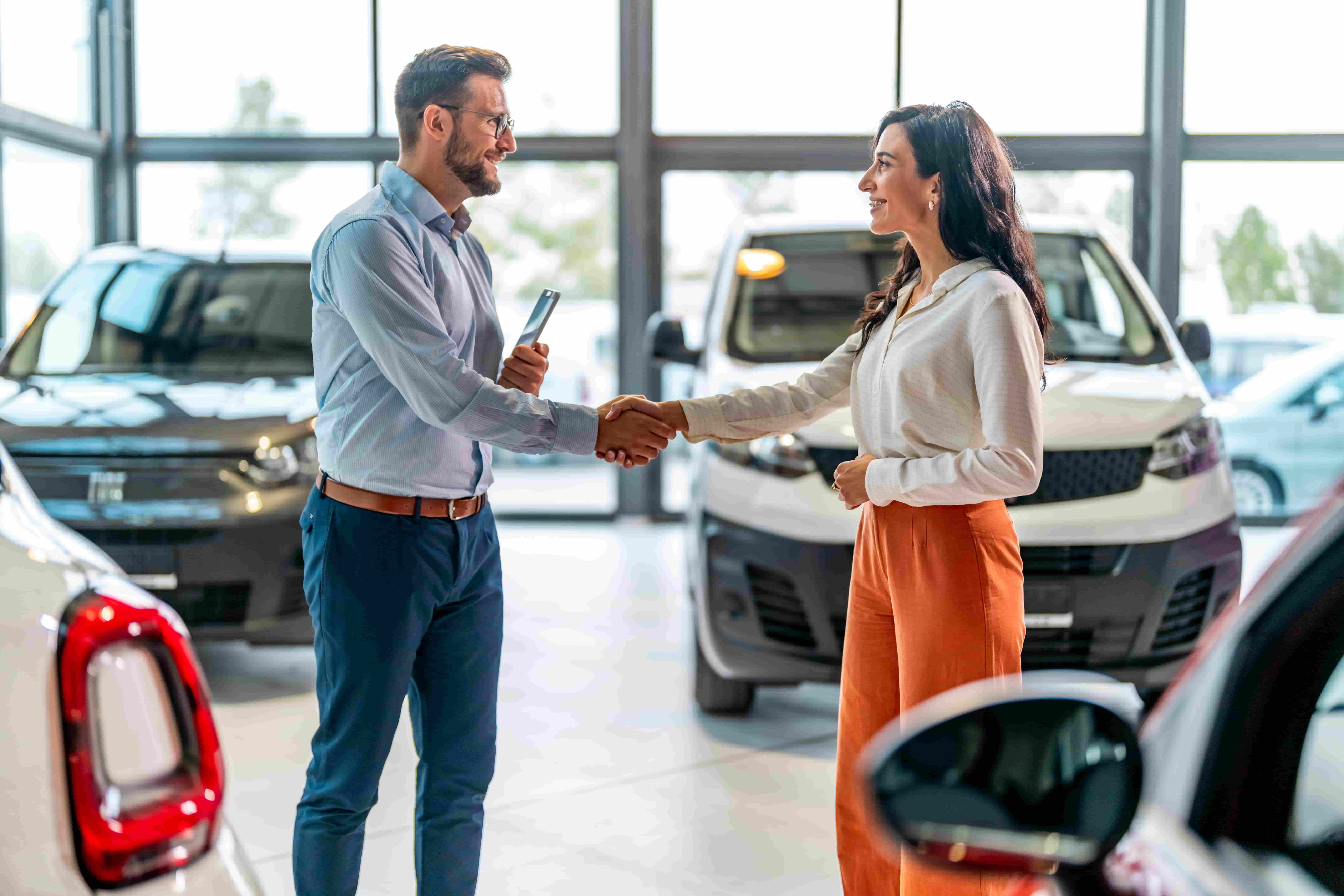 People shaking hands in front of cars