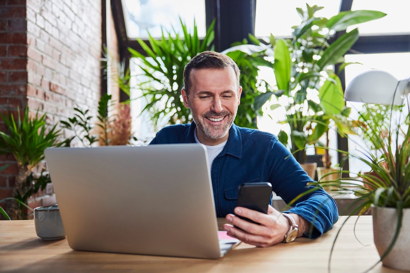 Man sitting at a desk with his laptop looking at a phone
