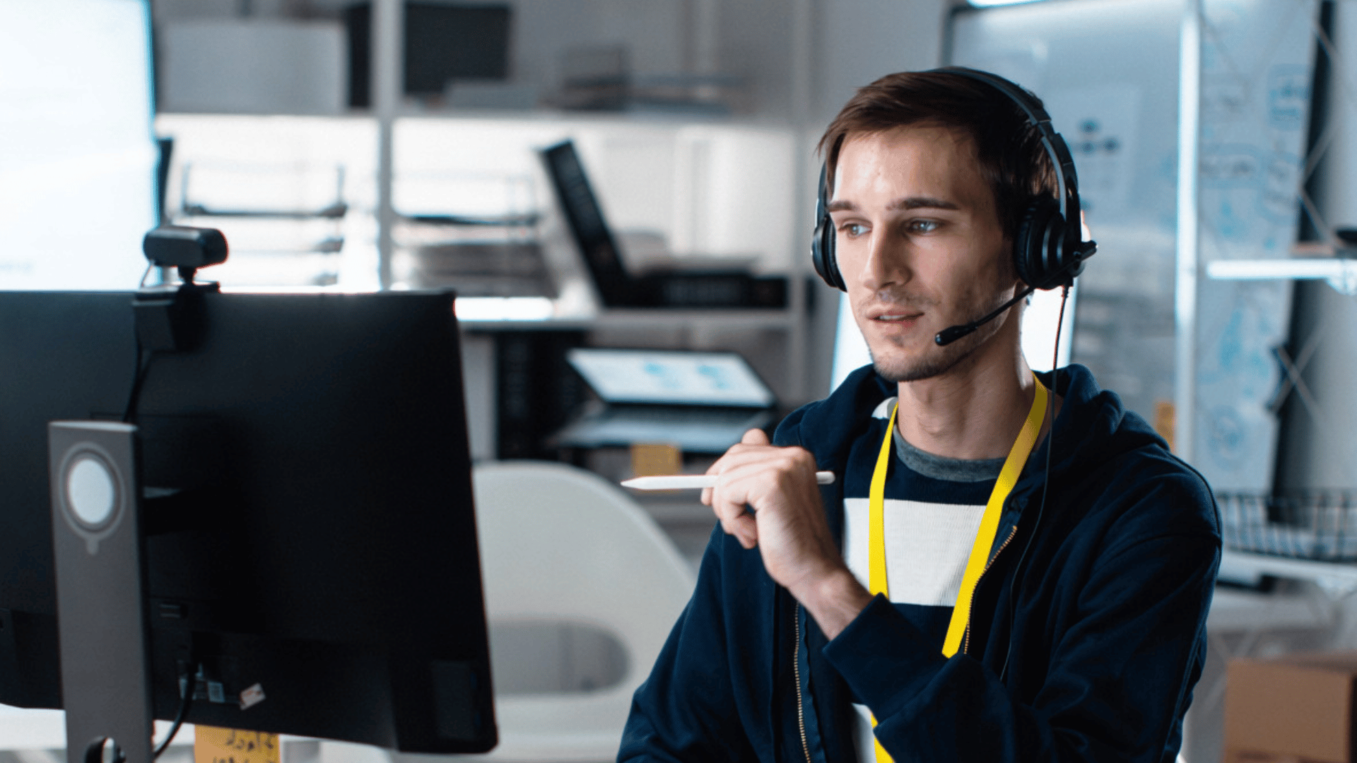 Male employee sat with headset on, pointing to computer screen.