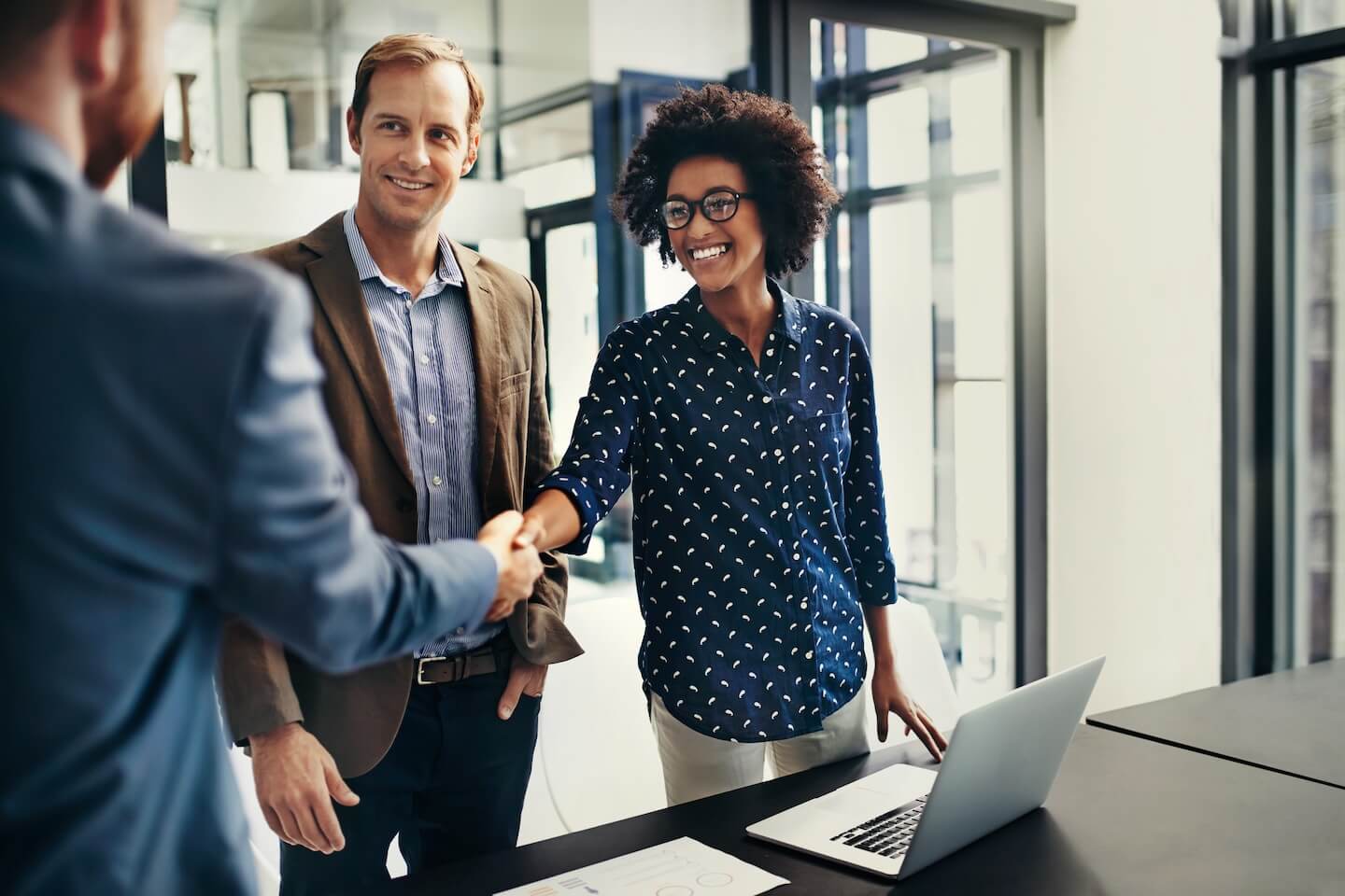 Woman with glasses smiling and shaking hands with man