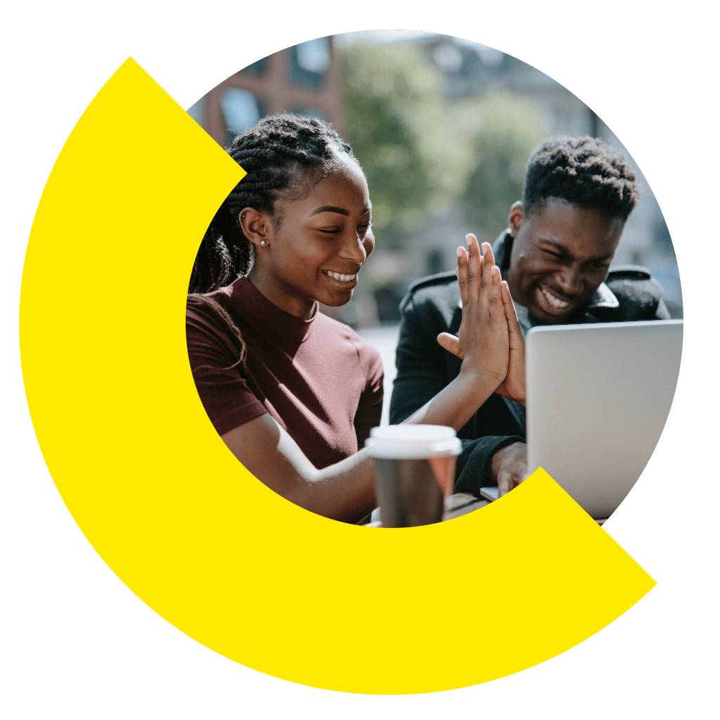 Two people sitting outdoors high fiving in front of a laptop.