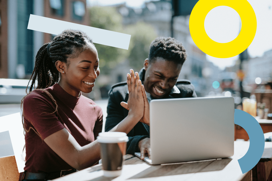 Two people seated outside high fiving in front of a laptop.