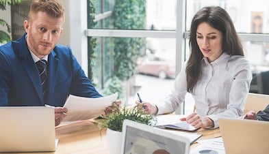 Two business professionals in a meeting with papers and laptops