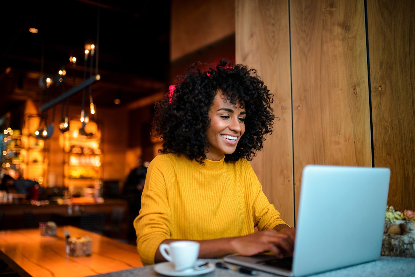 Woman working in a restaurant with her laptop and a coffee with remote access protected by zero trust technology