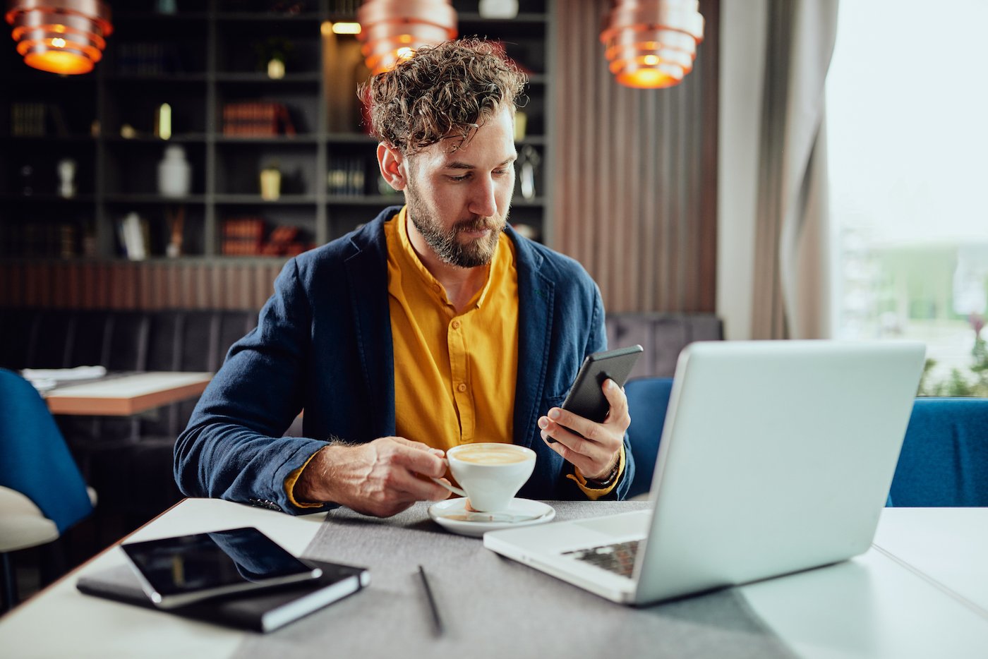Man at table with coffee using laptop and mobile device