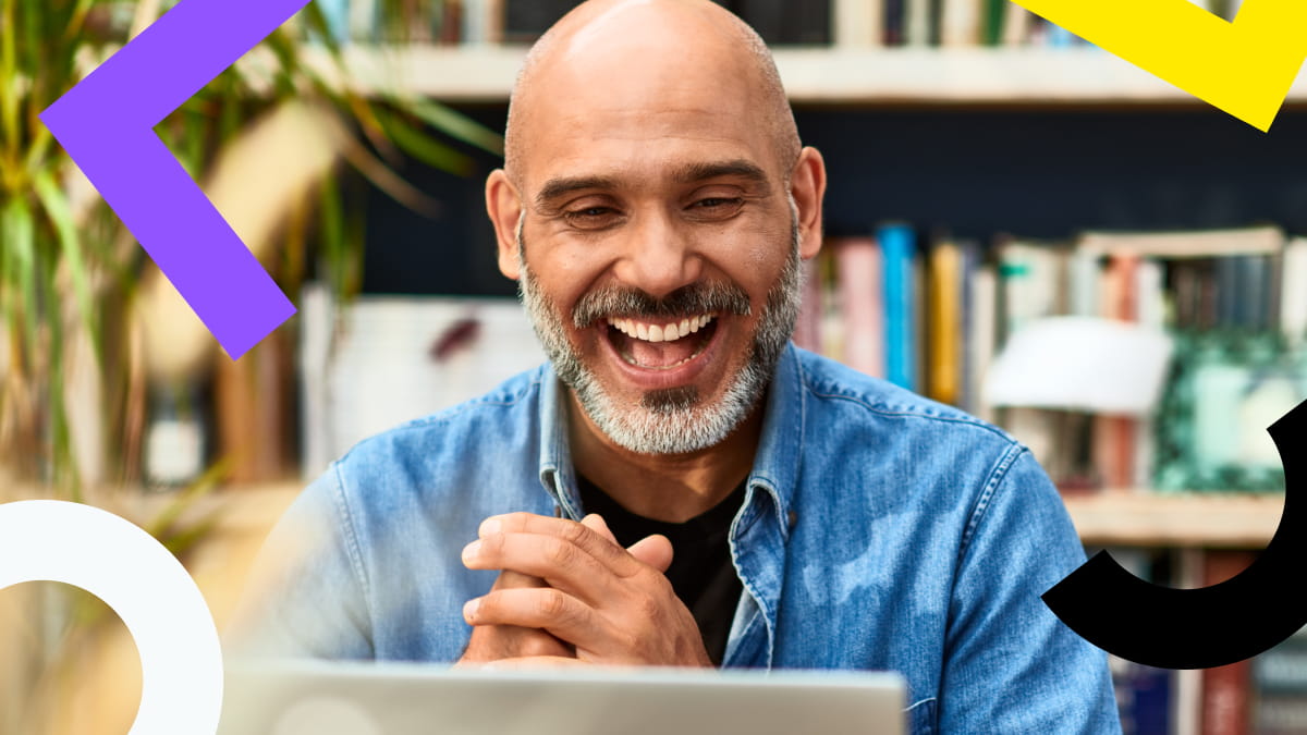 A smiling man working on a laptop in a casual office environment.