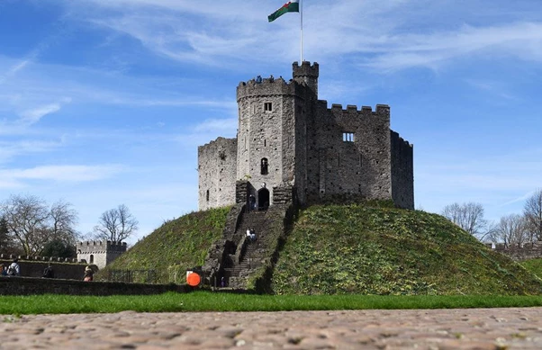 a stone castle with a flag on top of it with Cardiff Castle in the background
