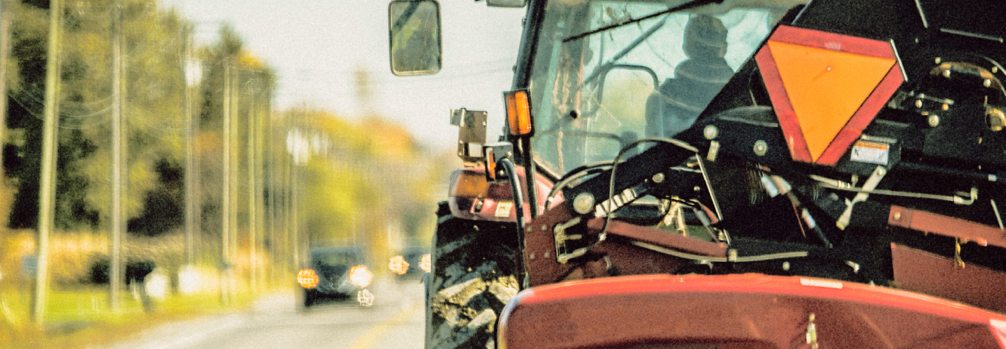 A large red tractor with a slow-moving vehicle sign drives on a rural road with oncoming traffic visible ahead.