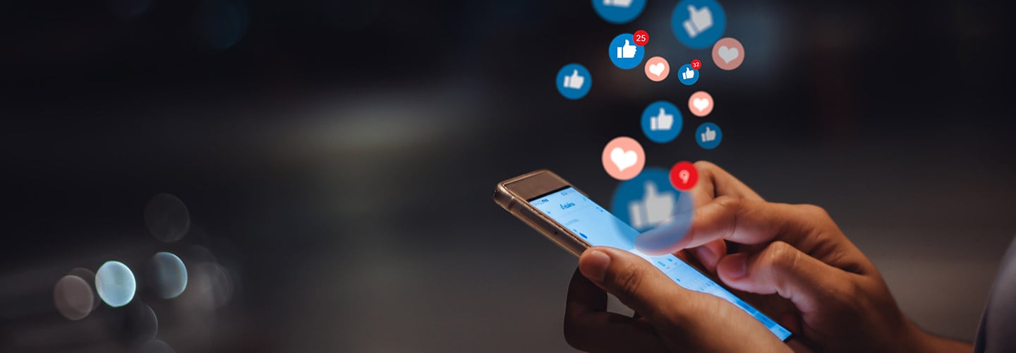 hands holding a cellphone with social media icons floating above the phone