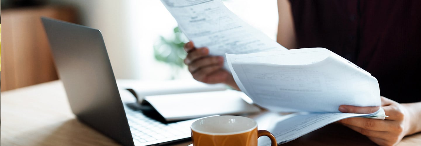 woman looking at papers with a laptop open on the table