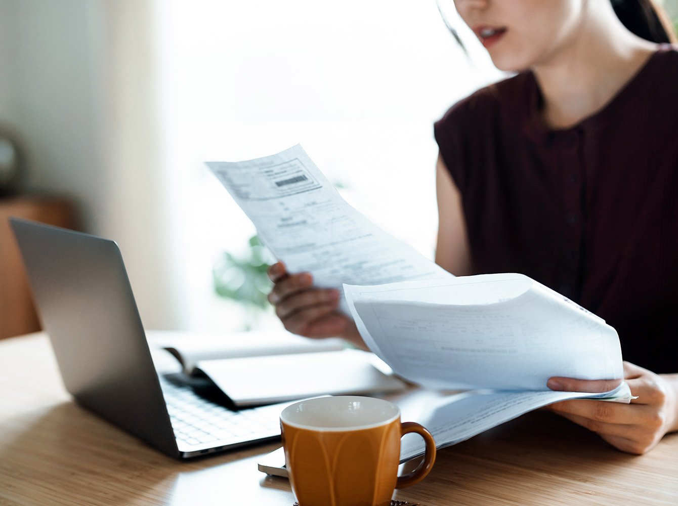 woman looking at papers with a laptop open on the table