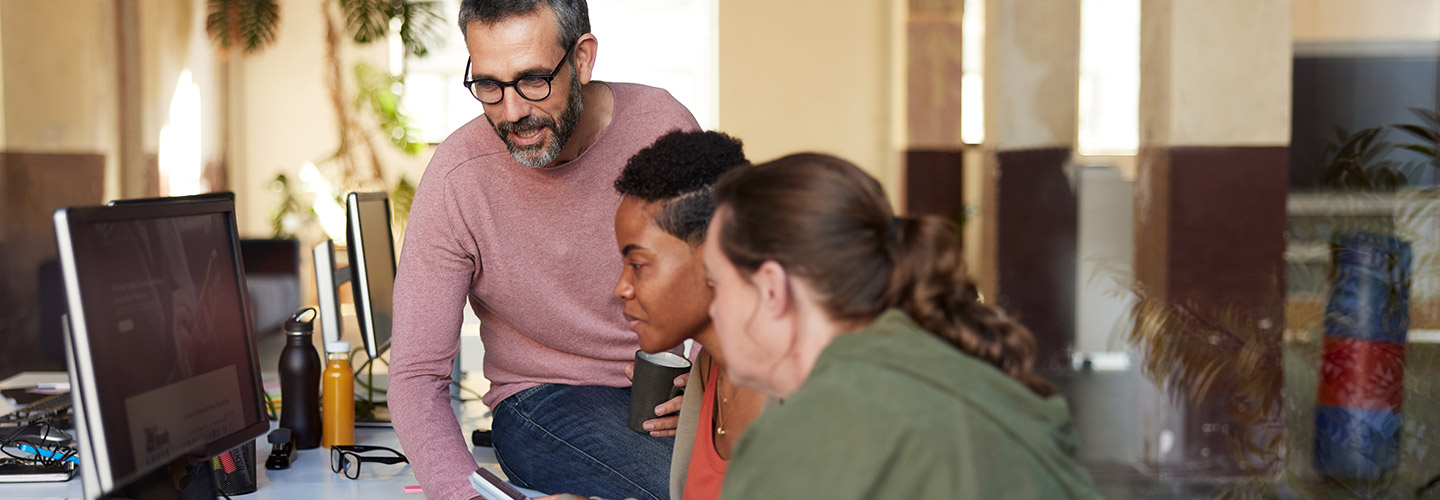 Employees gathered around a computer at a desk.