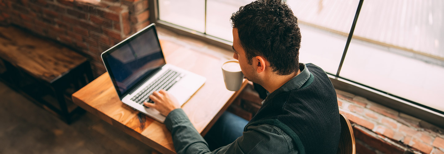 Man drinking coffee and typing on a laptop